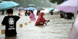 Menschen mit Regenschirmen bewegen sich durch hüfthohes Wasser