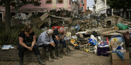Opfer der Flutkatastrophe sitzen erschöpft neben einem riesiegen Hausen Schutt in einer Häuserschlucht