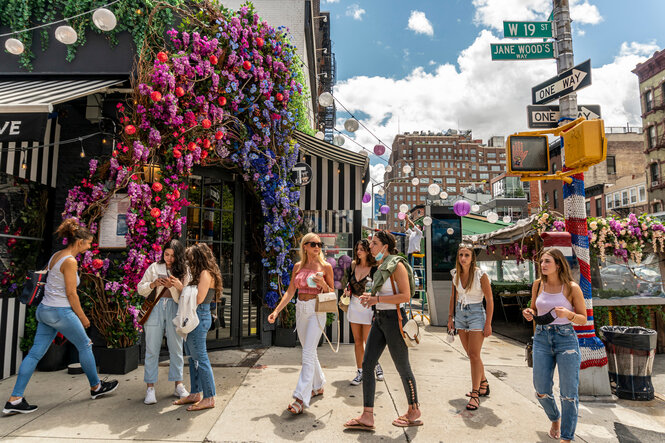 Junge Frauen an einer Straßenkreuzung in New York. Im Hintergrund ist der Außenbreich eines Restaurants zu sehen