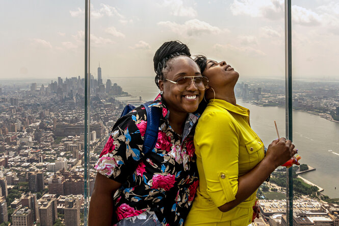 Zwei Schwarze Frauen lehnen sich auf einer Aussichtsplattform über New York aneinander