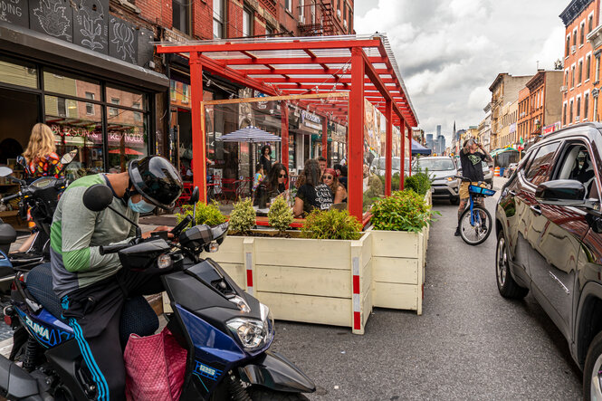 Ein Mann sitzt auf einem Moped. Dahinter ist der Außenbereich eines Restaurants zu sehen