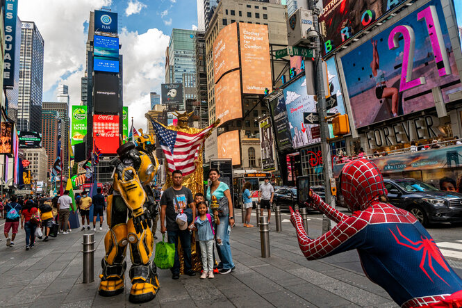 Eine als Spiderwoman verkleidete Frau zeigt auf ihre Familienmitglieder die als Roboter und Freiheitsstatue verkleidet sind