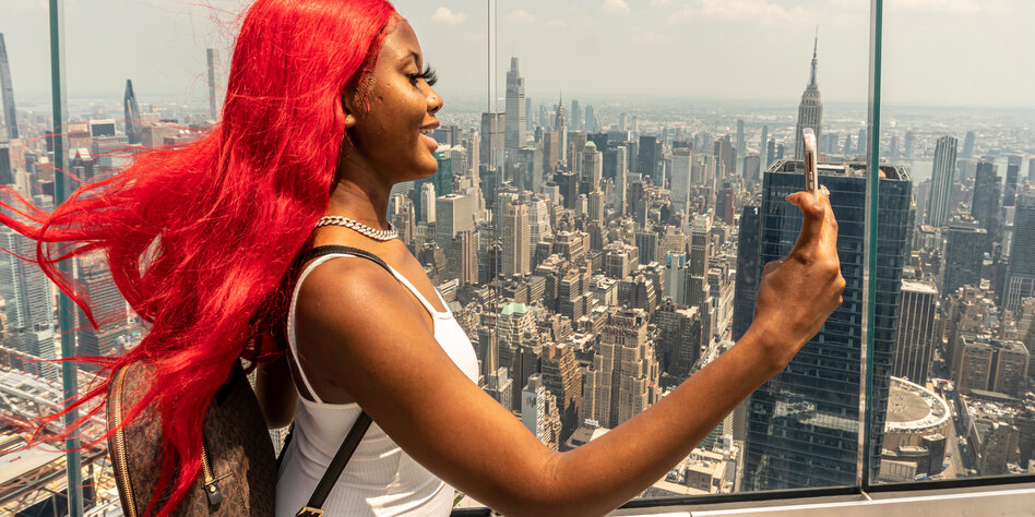 Eine Schwarze Frau mit roten Haaren macht ein Selfie vor der Skyline von New York