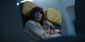 Eine verängstigte Frau hält einen blonden Jungen im Arm, während sie auf Sitzen im Flugzeug sitzen.