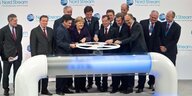 Gerhard Schröder une eine Gruppe internationaler Politiker (darunter Merkel, Öettinger und der französische Premierminister Francois Fillon) drehen an einem symbolischen Gasrad