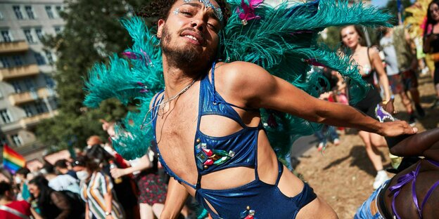 Eine queere Person tanzt in knappem Outfit und Feder-Schmuck