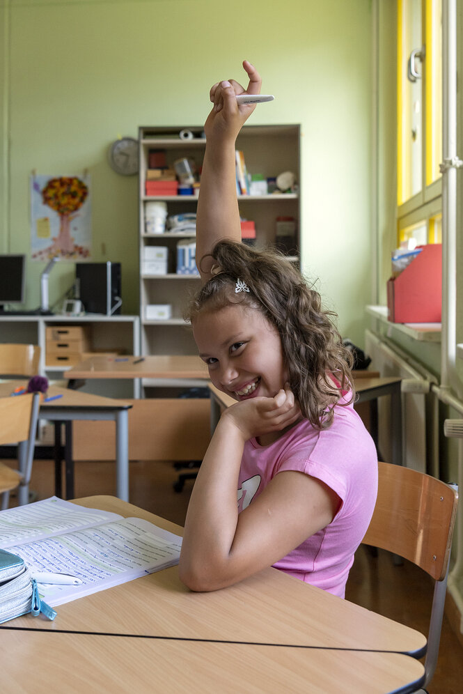 Ein Mädchen sitzt in einem Klassenraum und meldet sich: sie nimmt an einer Sommerschule in den Ferien in einer Grundschule in Berlin-Heiligensee teil