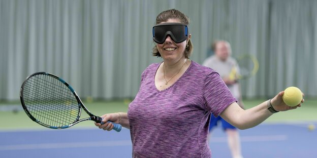 Christiane Kaplan hat einen Tennisschläger in der Hand und eine schwarze Brille über den Augen
