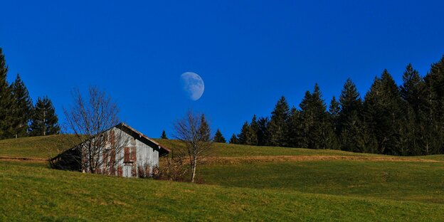 Eine Berghütte und der Mond am Himmel.