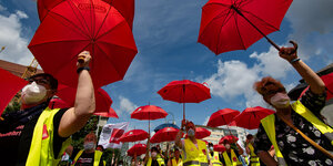 Menschen mit Verdi-Westen tragen aufgespannte Verdi-Regenschirme bei Sonnenschein