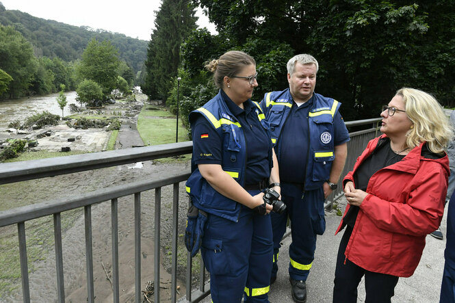 Schulze in roter Jacke, HelferInnen des THW in blauer Uniform vor der Wupper