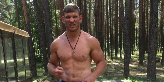 Alexej Kudin steht oberkörperfrei in einem Wald