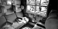 Blick in das Abteil eines Zuges, der von herabfallenden Trümmern stark beschädigt wurde. Auf Sitzen und dem Boden liegt Glas und Schutt.