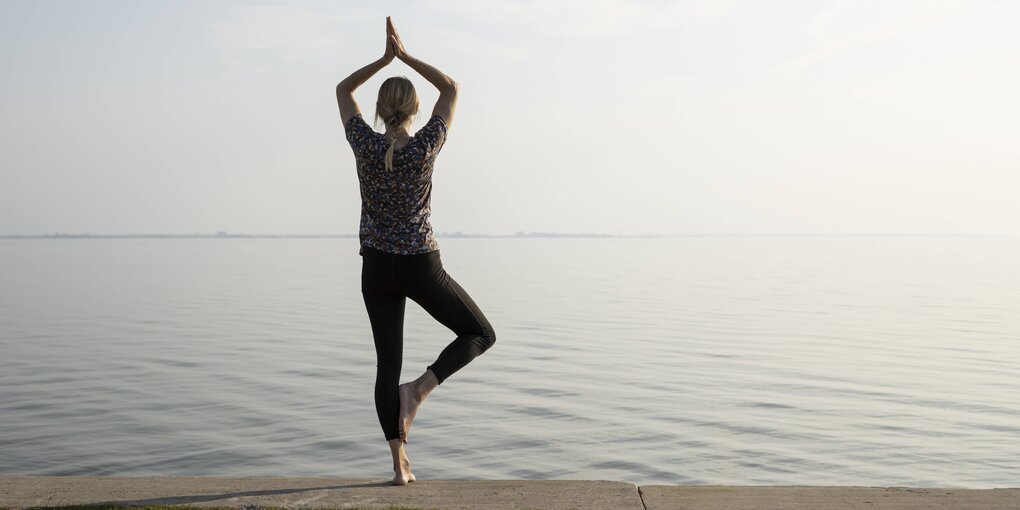 Frau macht die Yogastellung Baum an einem See