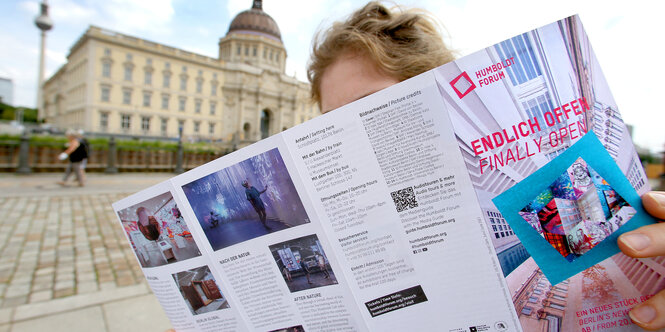 Eine junge Frau studiert vor dem Humboldt Forum eine Broschüre über das Ausstellungsangebot zur Eröffnung des Forums am 20. Juli - das Schloss ist im Hintergrund zu sehen