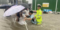 Ein Verkehrspolizist hilft Bewohnern von Zhengzhou durch die braunen Wassermassen