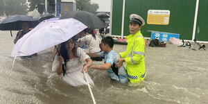 Ein Verkehrspolizist hilft Bewohnern von Zhengzhou durch die braunen Wassermassen