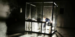 Grell erleuchteter Glaskasten auf dunkler Theaterbühne