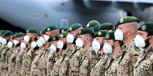 Mehrere Bundeswehrsoldat:innen stehen in einer Reihe, mit Mund/Nasenschutz, vor einer Transportmaschine