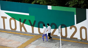 Hoher Bauzaun in grün-weiß mit goldener Aufschrift: Tokyo 2020. Zwei Männer gehen ihn entlang