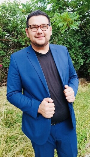Ein Mann mit blauem Anzug steht draußen vor einer Hecke Ein Mann mit blauem Anzug steht draußen vor einer Hecke