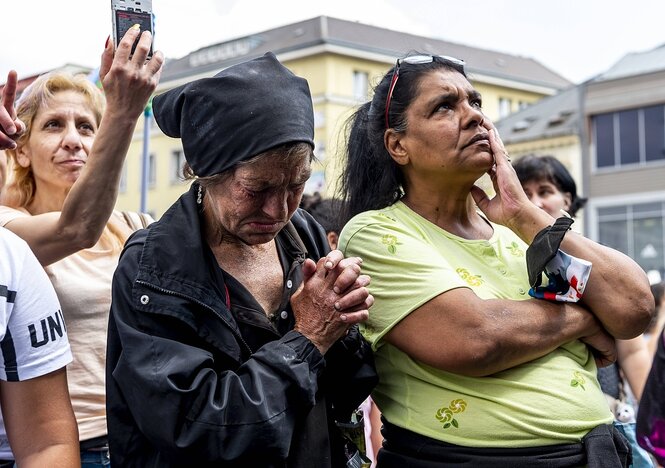 Das Bild zeigt mehrere Frauen bei einer Demonstration. Von den zwei vorn im Bild hat eine den Kopf gesenkt und die Hände gefaltet, die andere hat die Hand am Kinn und schaut nach oben