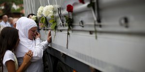 Eine Frau weint vor einem mit Blumen geschmückten LKW