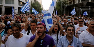 Hunderte Demonstranten mit griechischen Flaggen ziehen durch eine Straße und skandieren Parolen