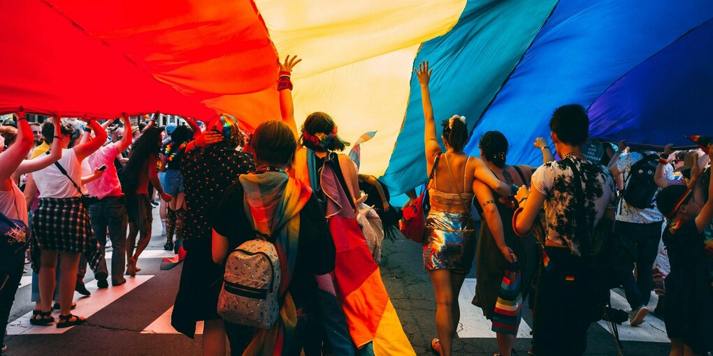 Menschen halten eine große Regenbogenfahne über sich