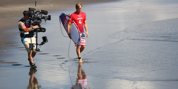 Ein Olympia-Surfer wird am Strand von einem Kameramann gefilmt.