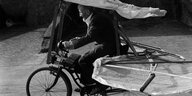 Schwarzweißes Foto von Gustav Messmer auf einem Fahrrad, an dem Flügel und Segel befestigt sind.