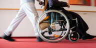 Ein Pfleger eines Pflegeheims schiebt eine Bewohnerin mit einem Rollstuhl.