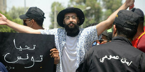 Ein Demonstrant hebt die Arme in die Höhe, im Vordergrund eine Sicherheitskraft