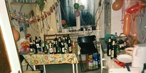 Nach einer Party stehen zahlreiche Bierflaschen auf einem Tisch in einer Küche, die mit Luftballons und Luftschlangen geschmückt ist