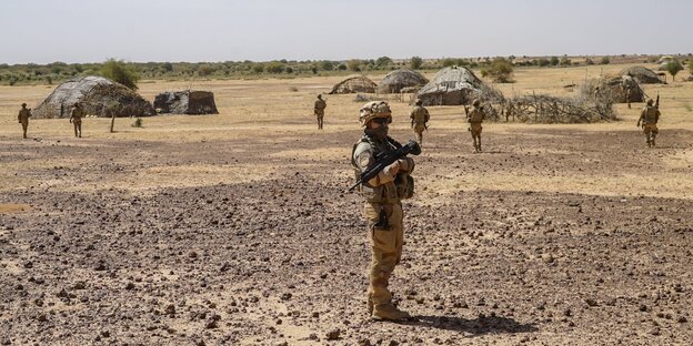 Ein französischer Soldat patroulliert in der Wüste, im Hintergrund Hütten eines Dorfes