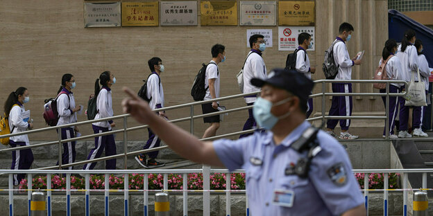 Polizist gestikuliert, während Schüler mit Mund-Nasen-Schutz Schlange stehen, um eine Schule für den ersten Tag der nationalen Hochschulaufnahmeprüfungen Chinas, bekannt als Gaokao, zu betreten
