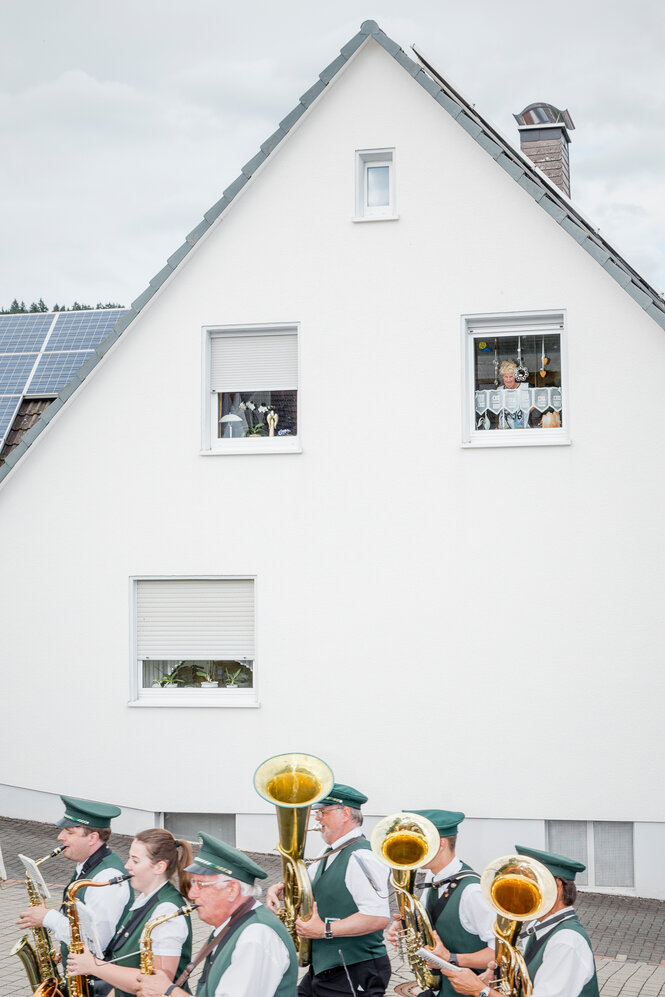 Eine Blaskapelle zieht an einem spitzgiebeligen Haus vorbei.