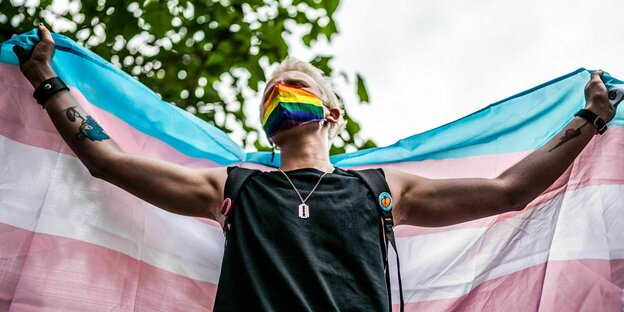 Person hält große Transgender-Flagge hoch (Querstreifen blau-pink-weiß-pink-blau)