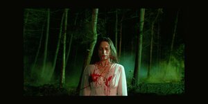Eine blutüberströmte Frau vor einem Wald