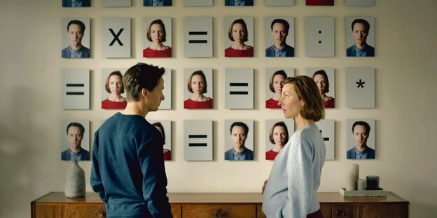 Die beiden Schauspieler:innen Tom Schilling (l.) und Katharina Schüttler (r.) stehen vor einer Wand, auf der sehr viele Fotos von ihnen abgebildet sind. Dazwischen stehen mathematische Zeichen wie Plus und Istgleich