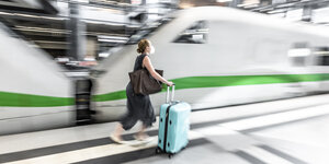 Frau rennt mit einem Koffer auf dem Bahnsteig ,dahinter ein ICE