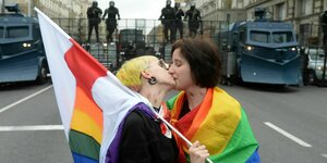 Zwei Personen mit Regenbogenflagge küssen sich