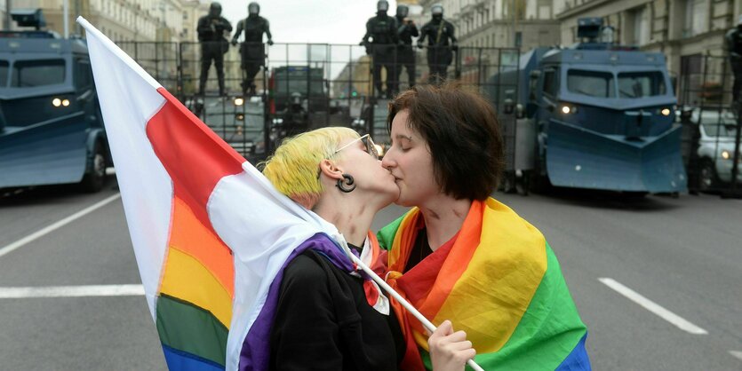 Zwei Personen mit Regenbogenflagge küssen sich