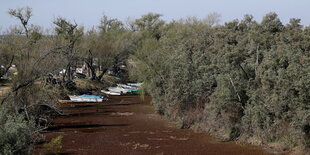 Das ausgetrocknete Flussbett, umrahmt von Vegetation. Boote liegen auf dem Grund