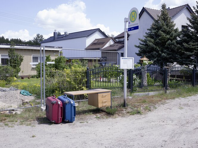 Eine Buswartehalle mitten in einer Wohnsiedlung in der Stadt Cottbus - ganz ohne Menschen, aber mit zwei Koffern und einem Schreibtisch