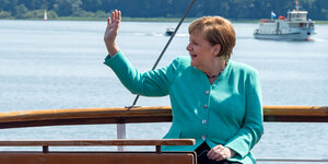 Angela Merkel sitzt auf einem Boot und winkt