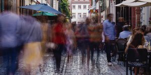 Verschwommene Silhouetten von Menschen laufen auf dem Kopfsteinpflaster in der Heidelberger Altstadt.