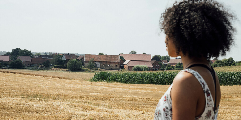 Eine Schwarze Frau von der Seite aufgenommen. Im Hintergrund ein Dorf