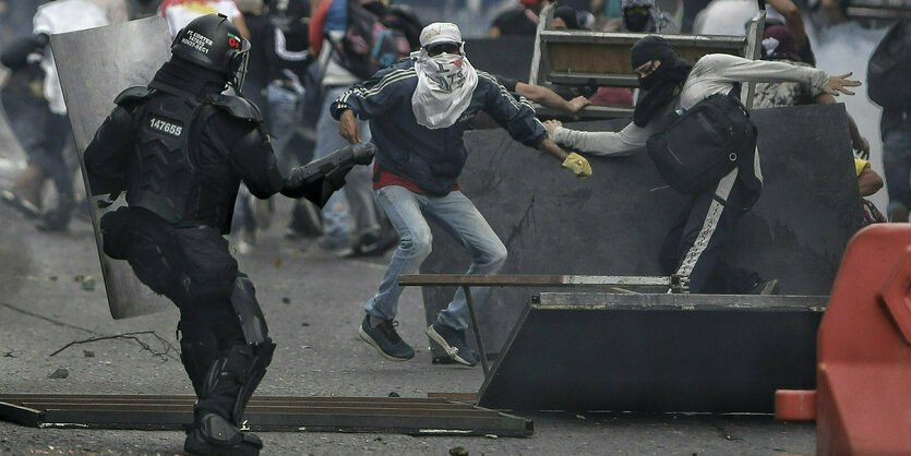 Verhuellte Demonstranten gehen vor einem Polizisten in Deckung