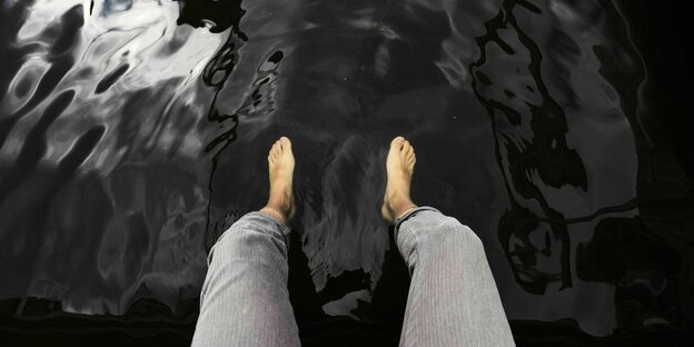 Mann sitzt auf einem Steg an einem See und lässt seine Füße im Wasser baumeln
